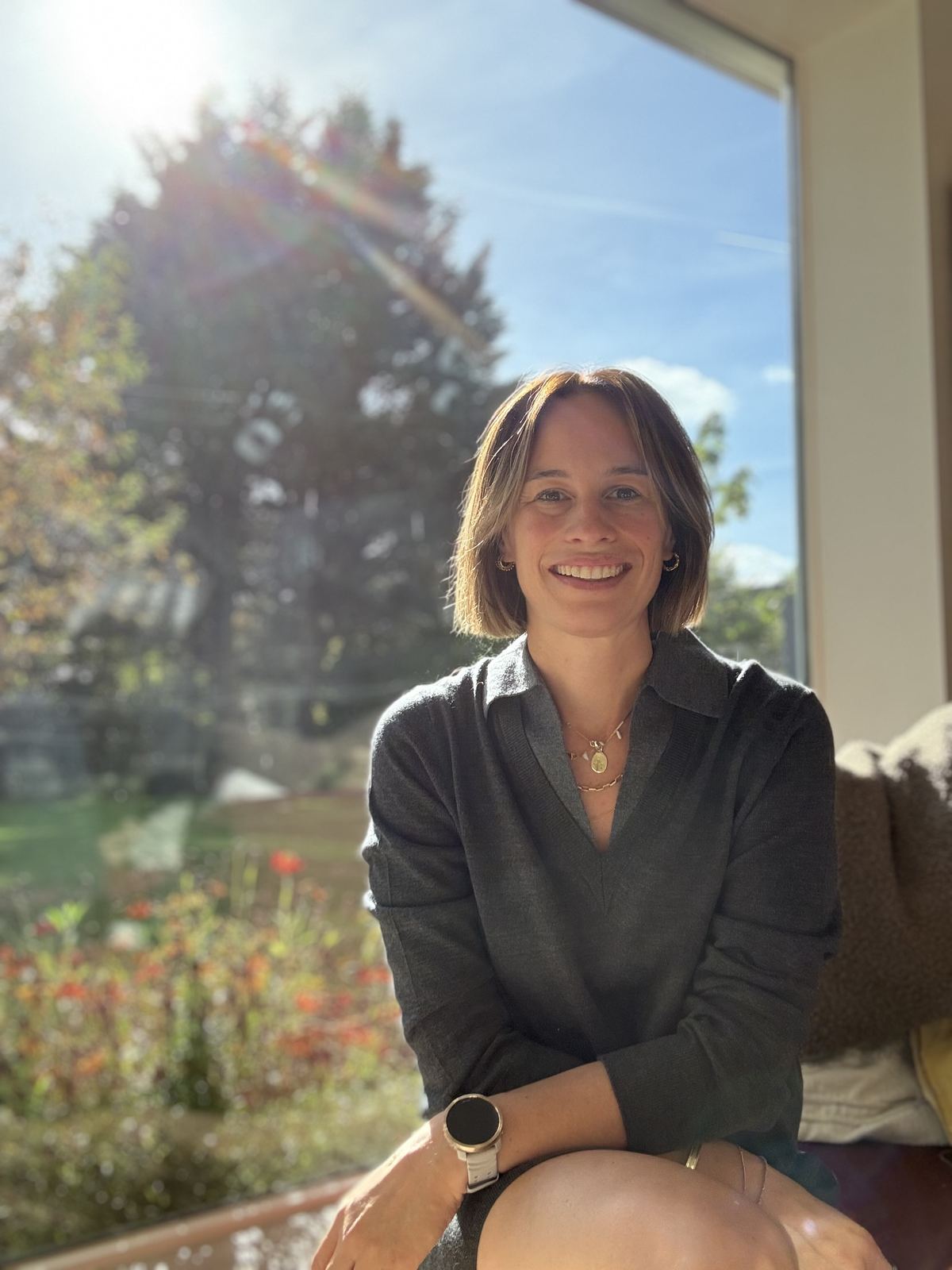 Judith glimlacht, zittend bij het raam in het zonlicht